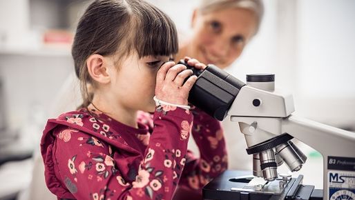 EB girl looking through a microscope in an EB lab.