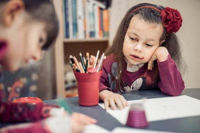 Two girls sit at a desk and draw