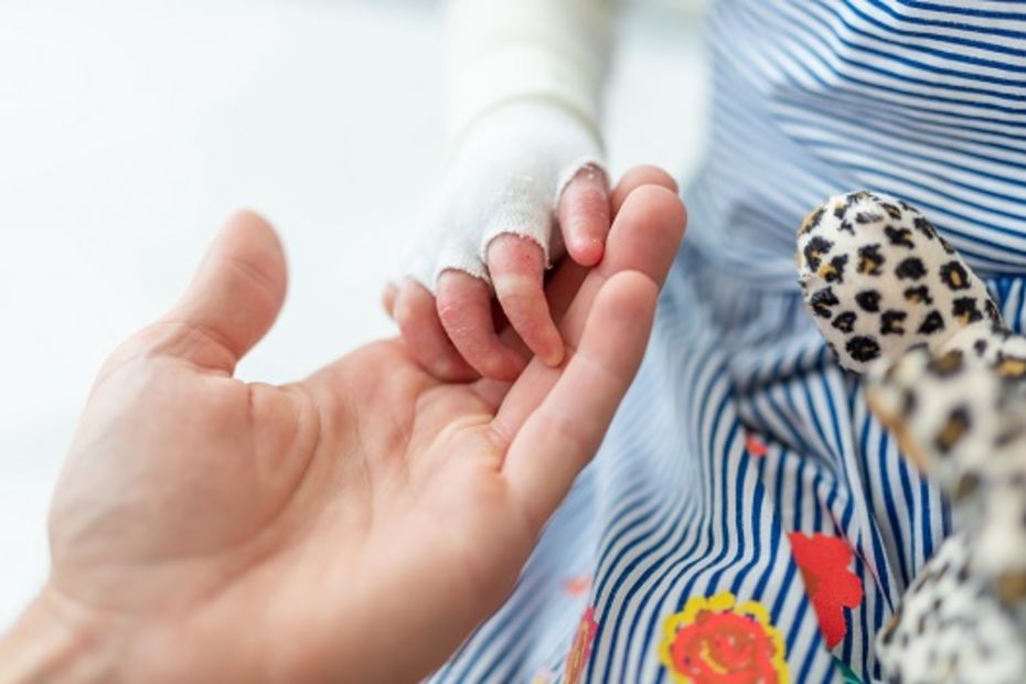 Close-up of an adult hand holding a child's hand with bandages