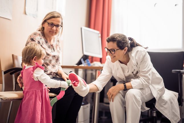 Doctor hands something to a little girl and her mother