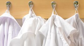 Four white coats hang on four wall hooks